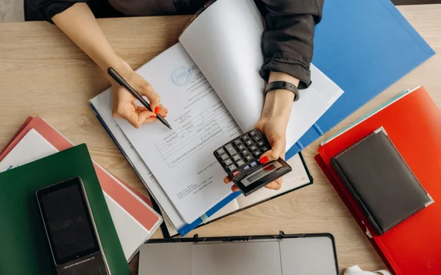 Persoană cu un calculator și documente pe birou