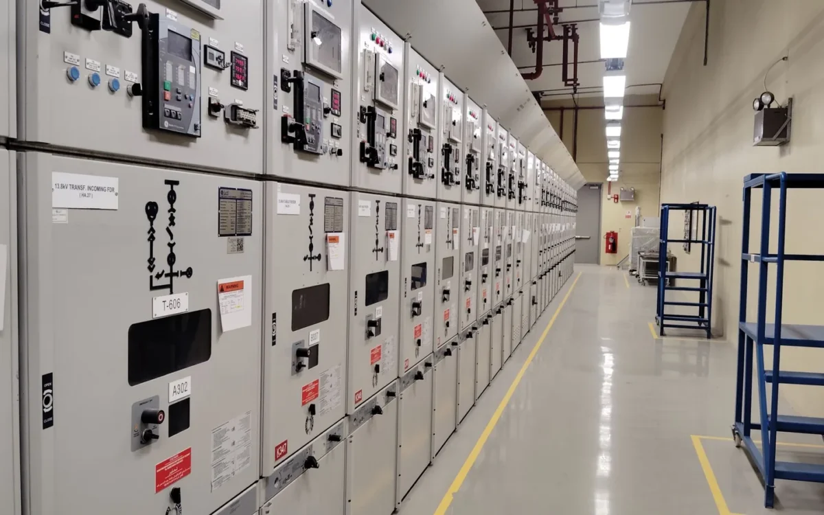 Șir de panouri electrice într-o încăpere industrială cu podea marcată cu linii galbene