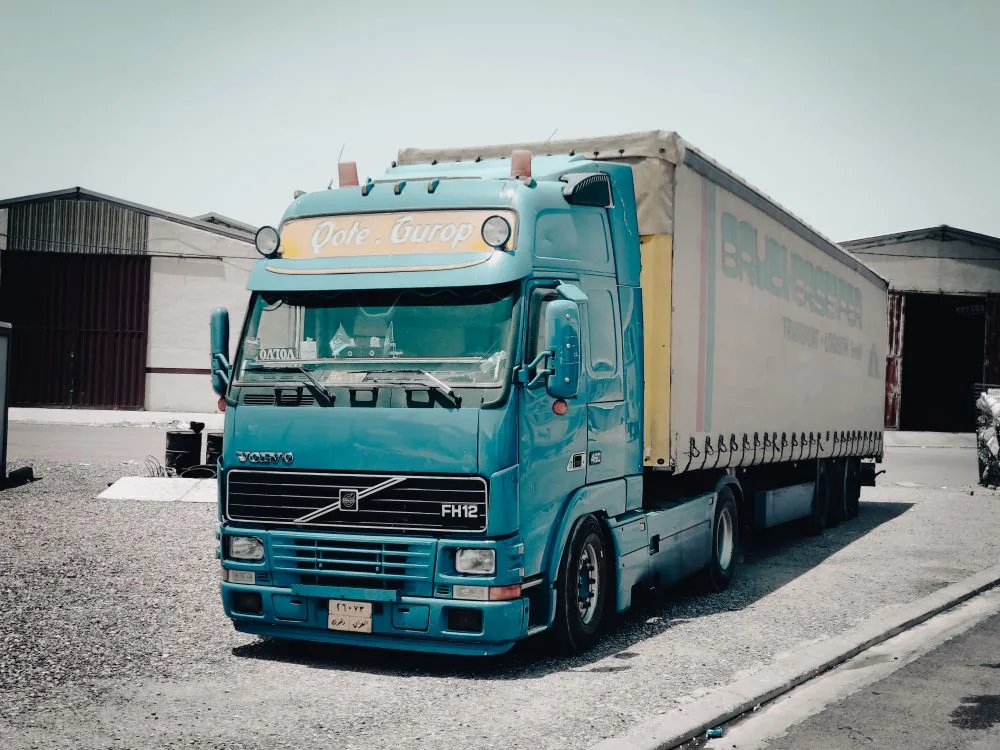 Camion Volvo albastru cu semiremorcă, în fața unor depozite
