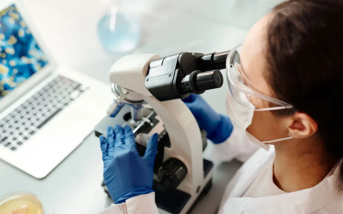 Cercetătoare cu echipament de protecție folosind un microscop în laborator