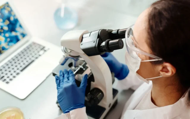 Cercetătoare cu echipament de protecție folosind un microscop în laborator