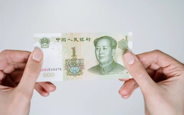 Două mâini țin o bancnotă chinezească de un yuan pe fundal deschis